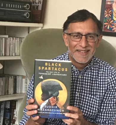 Sudhir Hazareesingh holding a copy of Black Spartcus, sitting in a green arm chair